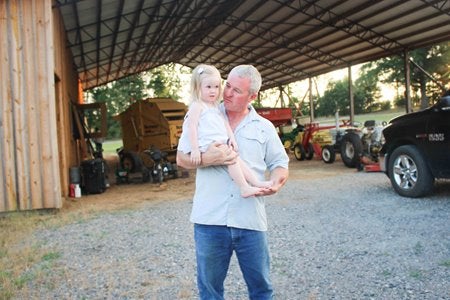 Man holding a baby in front of some farming equipment