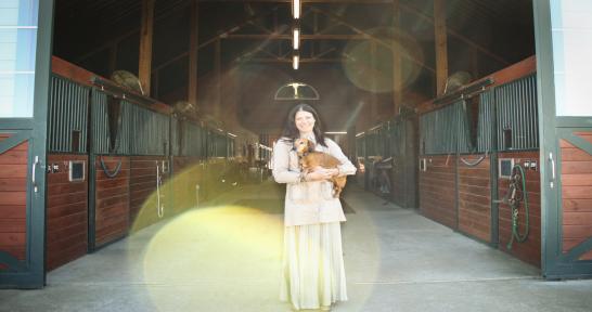 Mary Guynn holds her dog in the entrance to a horse barn